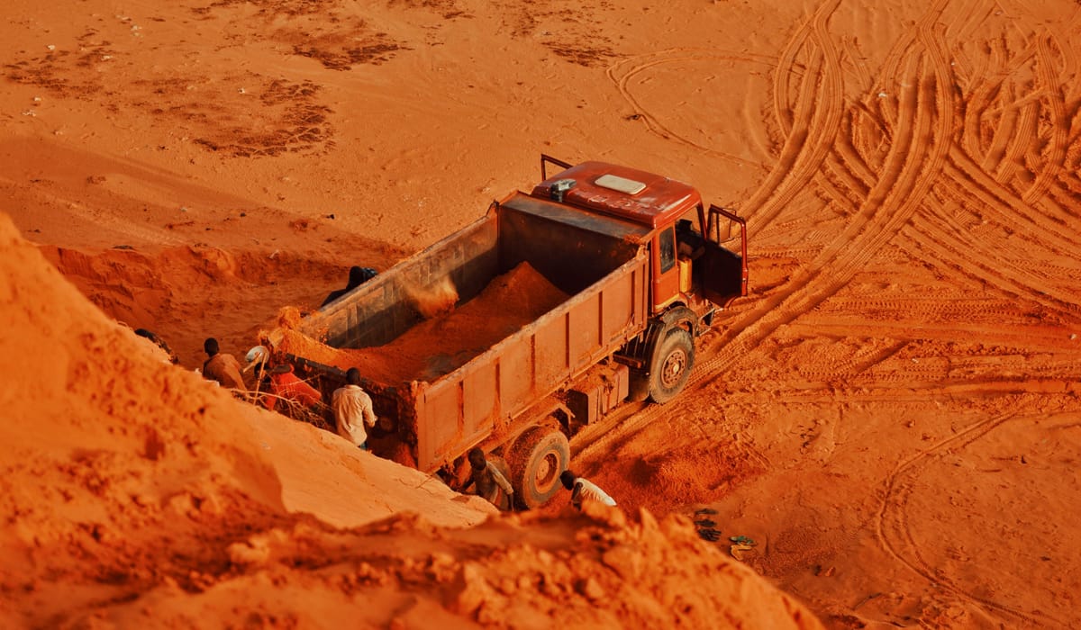 Camion benne chargé de latérite dans une carrière de terre rouge, des ouvriers à la pelle