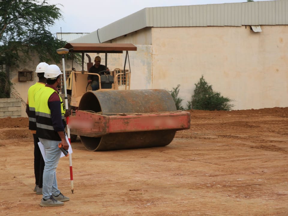 Deux chefs de chantier casqués devant un compacteur au travail