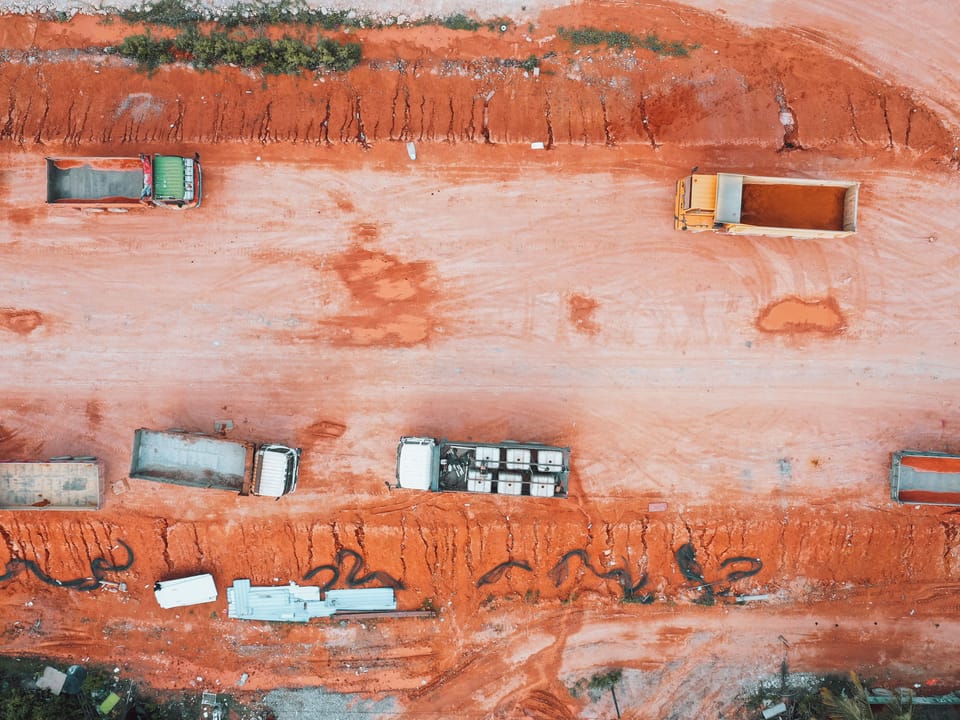 Camions bennes sur une piste de terre rouge, vus du ciel